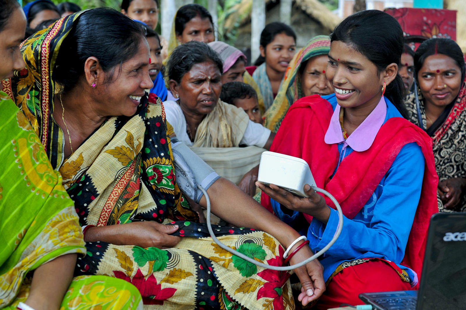 A woman in medical uniform is checking the blood pressure of other woman and there are other women sitting in the background A woman in medical uniform is checking the blood pressure of other woman and there are other women sitting in the background