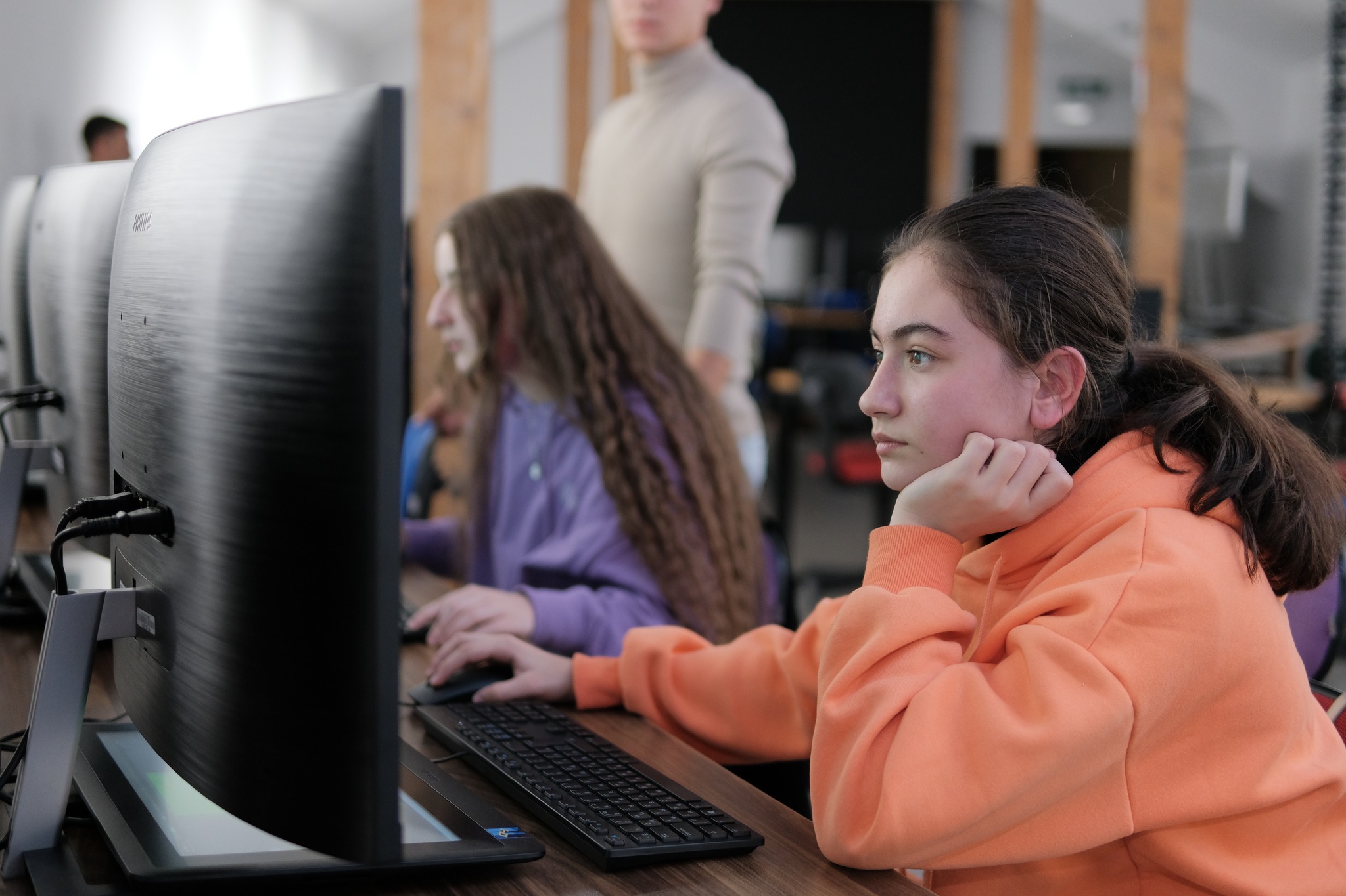 Girl in orange hoodie sitting in front of a computer Girl in orange hoodie sitting in front of a computer